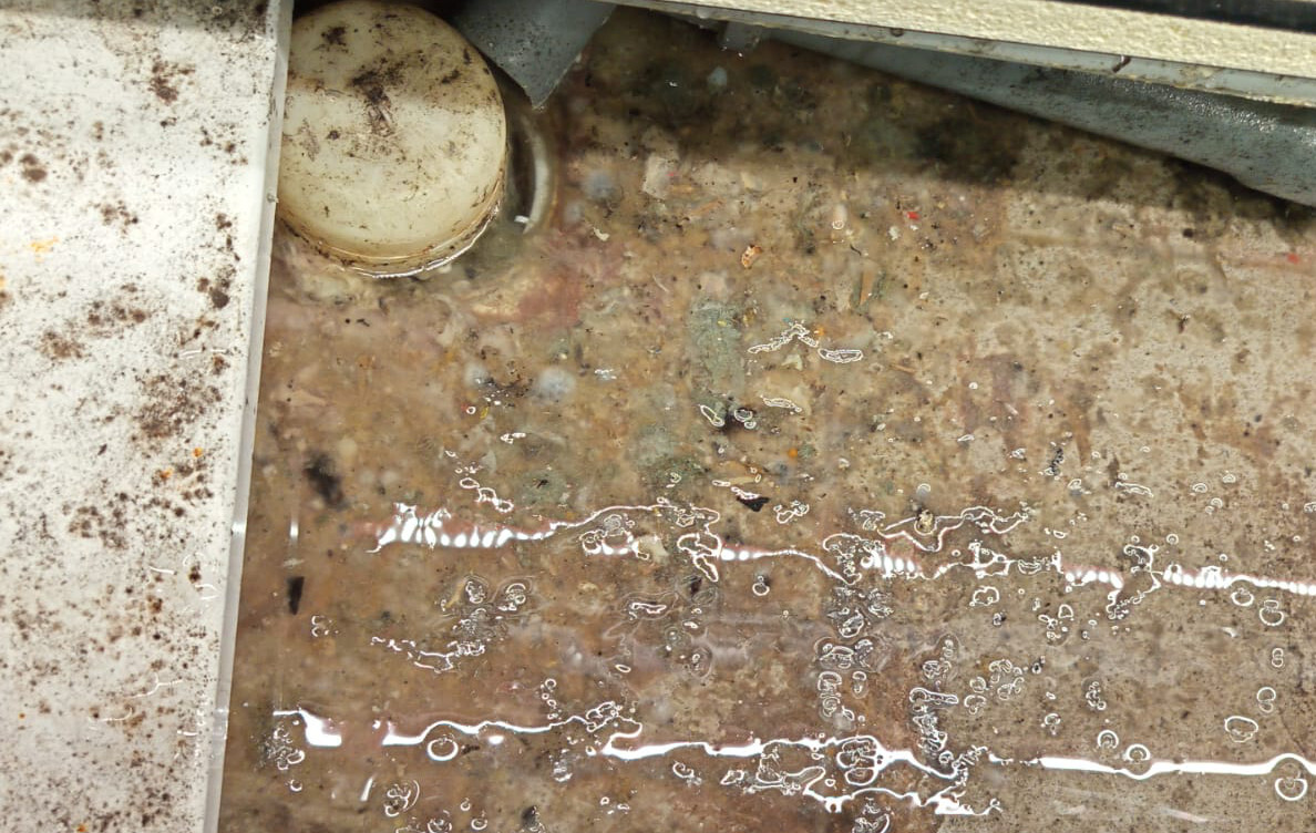 Zanieczyszczona chłodnia Zanieczyszczona chłodnia w sklepie spożywczym — widoczna brudna woda, osad i zabrudzenia na metalowych i plastikowych elementach.